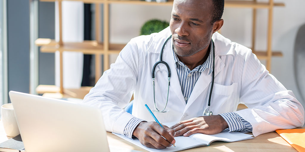 Doctor looking at computer and writing in his notebook